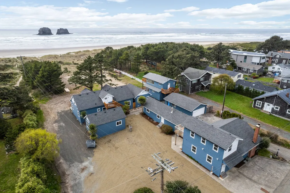 This image shows a tranquil beachfront scene with sandy shores, striking rock formations, and several cozy houses surrounded by trees. The scene evokes a feeling of serenity and offers a direct visual connection between the accommodations and the inviting oceanfront, with the possibility of watching sunsets or enjoying a walk by the shore.