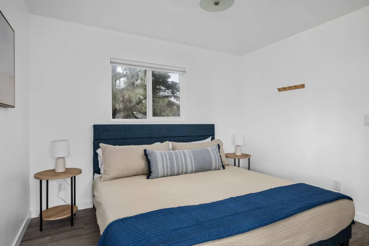 A serene bedroom highlighted by a plush king bed with crisp linens, flanked by nightstands and accented with decorative artwork. Natural light filters through the window, enhancing the tranquil and inviting mood.