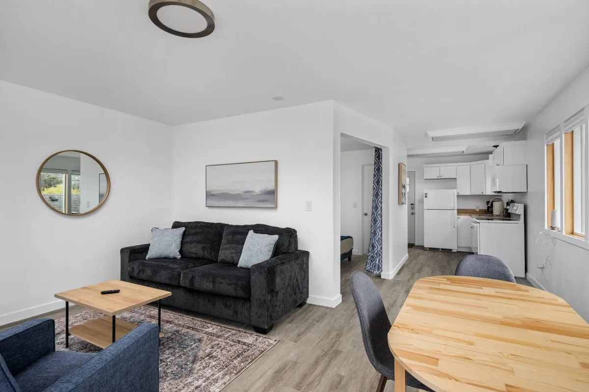 A cozy living area featuring a comfortable sofa, a dining table, and a large mirror that reflects the room’s airy light. The layout is inviting and flexible for relaxation or socializing.
