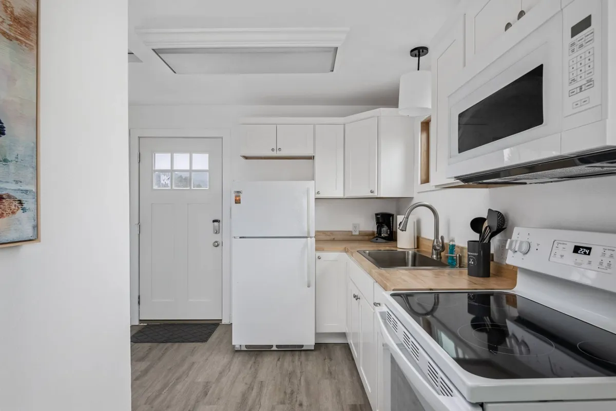 A bright, contemporary kitchen with white cabinetry, stainless steel appliances, and a wooden countertop. Ample natural light streams in, and the space feels both modern and welcoming, encouraging group meal prep or casual breakfasts.