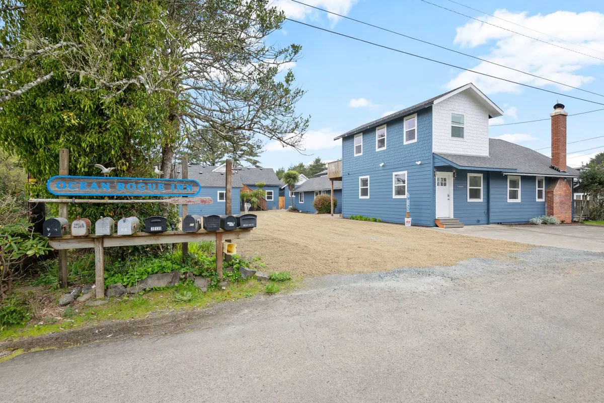 An inviting exterior shot of a blue house with clear signage and a cozy mailbox, surrounded by open outdoor space ideal for mingling. The mood is relaxed, with people casually chatting and preparing for local adventures or events, echoing the friendly resort vibe.