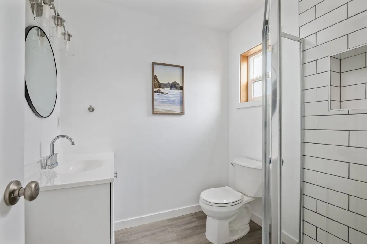 A modern bathroom with a glass shower enclosure, round mirror, and tasteful decorative touches. The tranquil atmosphere invites relaxation and rejuvenation.