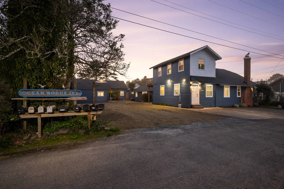 This image displays the Ocean Rogue Inn's charming exterior, including the entrance, its cozy sign, and surrounding greenery. The inviting facade hints at the thoughtful hospitality and welcoming atmosphere awaiting inside, and the setting sun in the background suggests evening relaxation and shared moments.