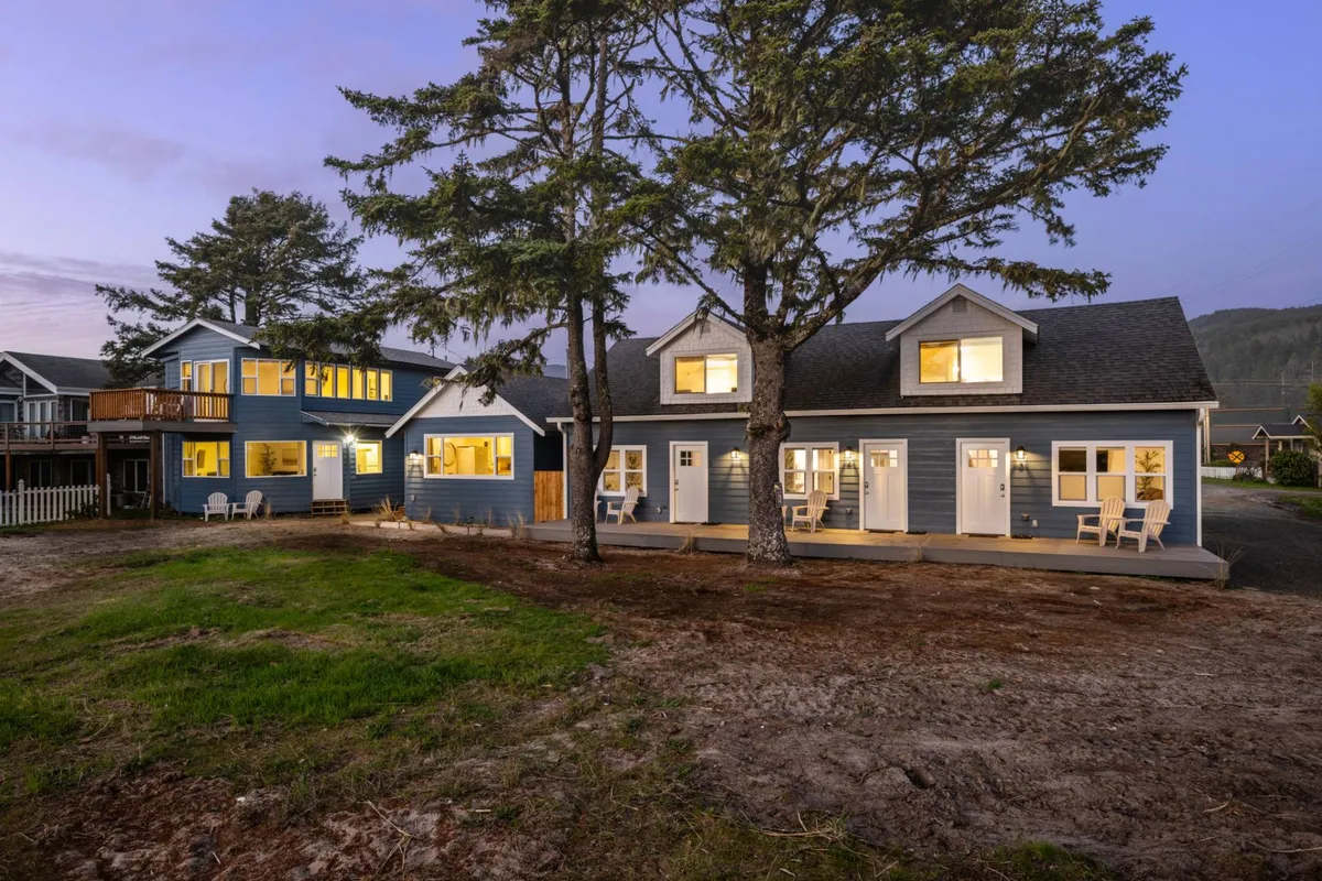 A spacious front yard with an inviting porch furnished with comfortable chairs and large windows reflecting the sunset. The scene hints at evening gatherings, outdoor relaxation, and the warmth of storytelling after a day of adventure.